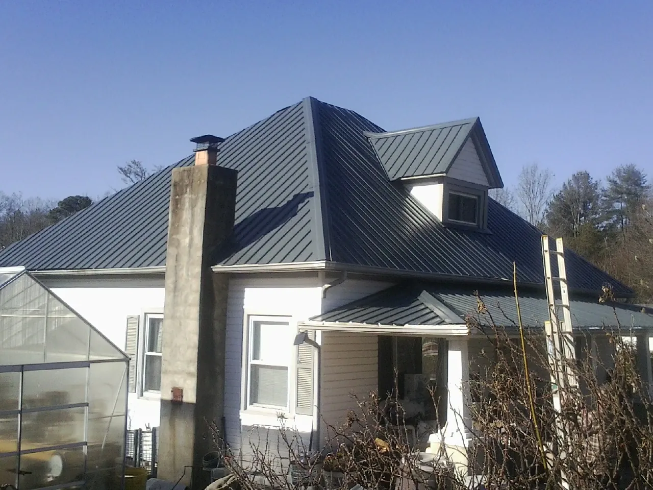 Dark blue standing seam metal roof on a white farmhouse with dormer — Slate & Tile Roof Repair by Roofing Brothers in Browns Valley