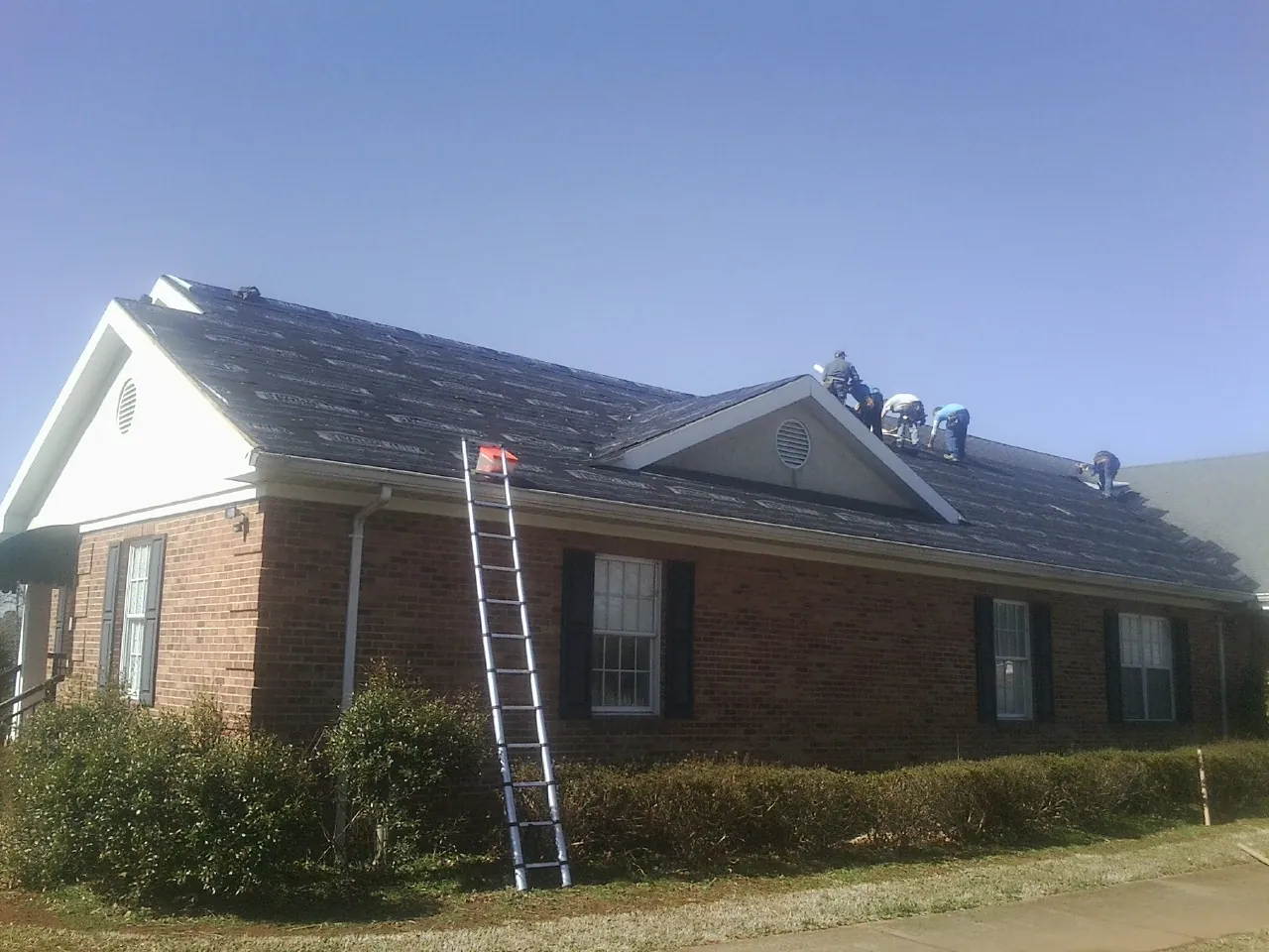 Crew tearing shingles off a brick ranch roof with a ladder set — Emergency Roof Repair work by our crew in Browns Valley