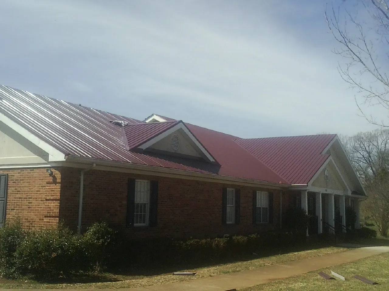 Red metal roof with gabled entries on a long brick building, from a Hail Damage Roof Repair job in Browns Valley