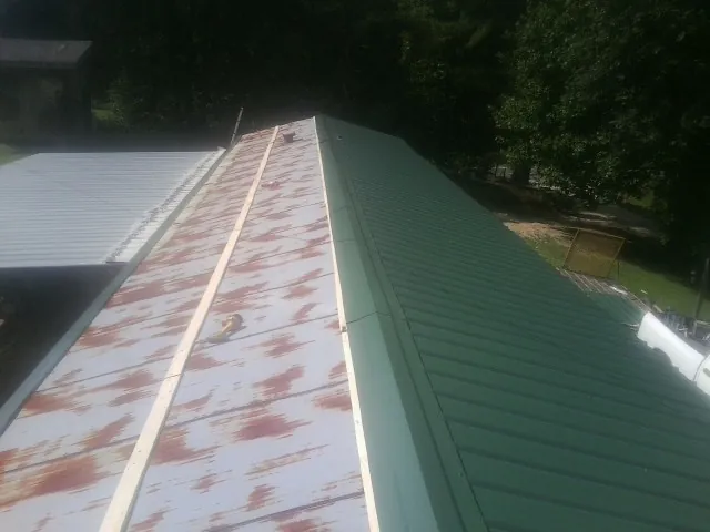 Old rusted panels beside newly installed green metal roofing — Wind Damage Roof Repair by Roofing Brothers in Browns Valley