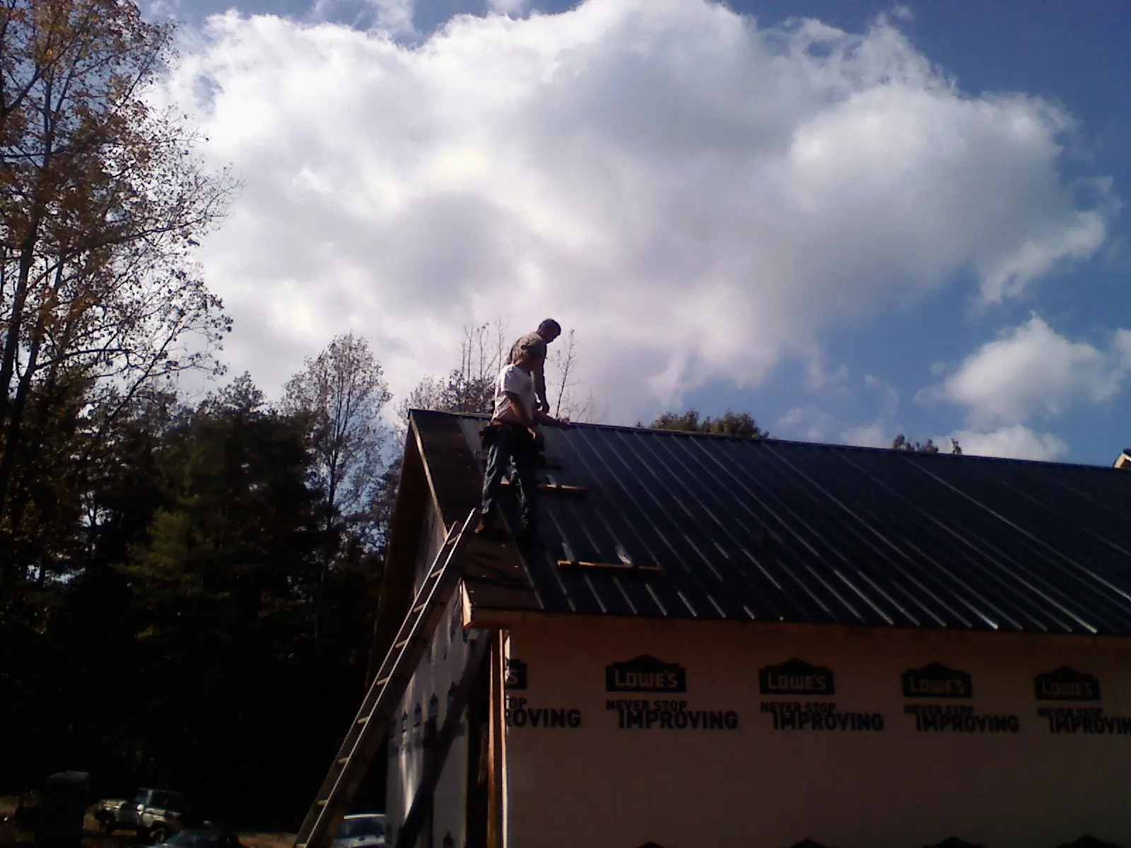 Roofer fastening dark metal panels high against a cloudy sky, from a Roof Inspection job in Browns Valley