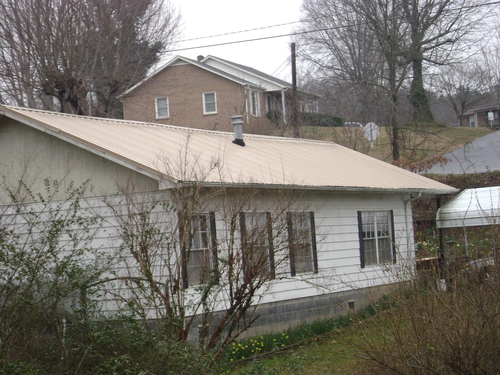 Tan metal roof on a white sided house set into a hillside — Commercial Roofing by Roofing Brothers in Browns Valley